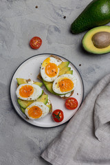 Burger on grain bread with boiled egg and avocado on plate on gray background