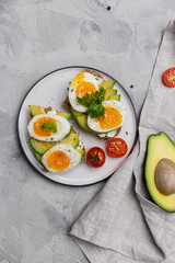 Burger on grain bread with boiled egg and avocado on plate on gray background