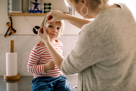 Mother applying bandage on daughter's face at home