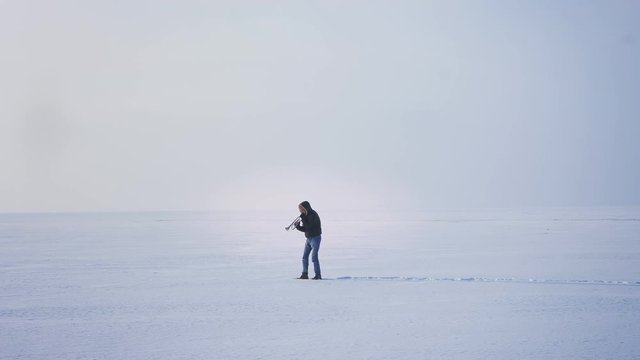 Wide shot of alone caucasian musician playing trumpet putting it up and down on frozen lake background.