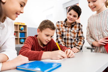 Smiling pupils with notebooks and books discussing in classroom