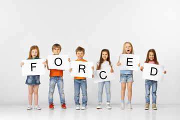 Obraz premium Being forced is prison. Group of angry screaming children with a white banners holding word isolated in studio background. Education, advertising and social rights concept.