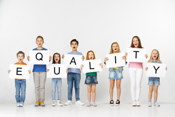 Equality gives us friendship. Group of smiling and screaming children and teenagers or young team with a banners holding word isolated in white studio background. Education and advertising concept.