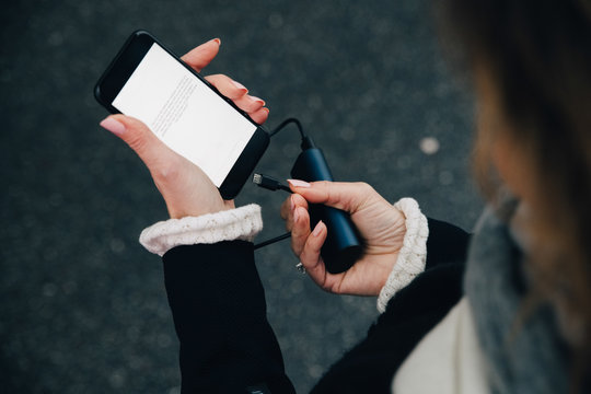 Midsection of businesswoman inserting charger in mobile phone while standing on road