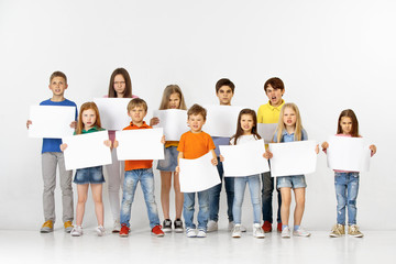 Group of angry children with a white empty banners isolated in studio background. Education and advertising concept. Protest and children's rights concepts.