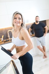 Fitness woman in kitchen, man in background. Husband and wife cooking together.