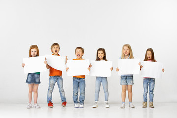 Obraz premium Group of angry screaming children with a white empty banners isolated in white studio background. Education and advertising concept. Protest and children's rights concepts.