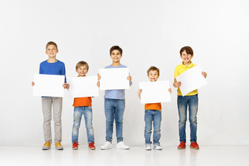 Obraz premium Group of happy children with a white empty banners isolated in light studio background. Education and advertising concept