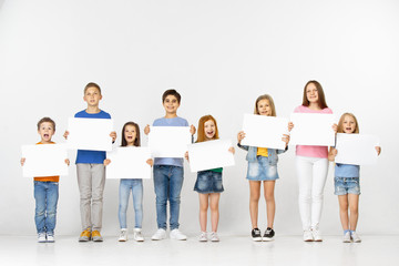 Obraz premium Group of happy smiling children with a white empty banners isolated in light studio background. Education and advertising concept