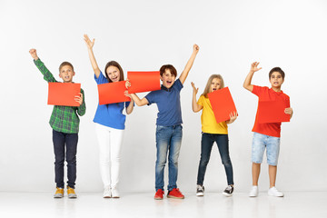 Fototapeta premium Group of happy smiling children with red empty banners isolated in white studio background. Education and advertising concept