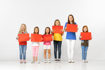 Obraz premium Group of happy smiling children with red empty banners isolated in white studio background. Education and advertising concept