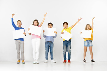 Obraz premium Group of happy surprised children with a white empty banners isolated in white studio background. Education and advertising concept