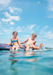 Little sister and brother sit on inflatable mattress in the sea. Happy summer holidays concept image.