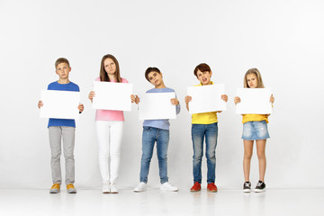 Obraz premium Group of sad serious children with a white empty banners isolated in white studio background. Education and advertising concept