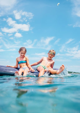 Little sister and brother sit on inflatable mattress in the sea. Happy summer holidays concept image.