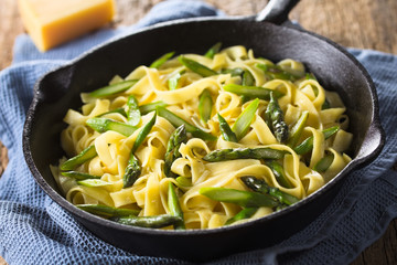 Fresh homemade pasta dish of fettuccine or tagliatelle, green asparagus, garlic and lemon juice in cast iron skillet (Selective Focus, Focus one third into the frying pan)