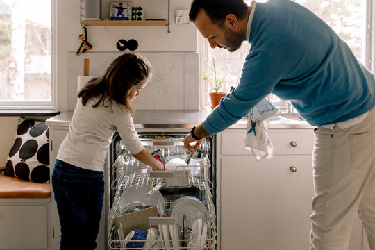 Father and daughter arranging utensils in dishwasher at kitchen