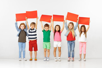 Group of unhappy sad children with red empty banners isolated in white studio background. Education and advertising concept. Protest and children's rights concepts.