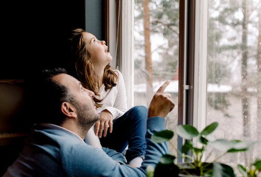 Father and daughter looking through window at home