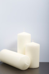 Candles white in different sizes. White background turning into dark.