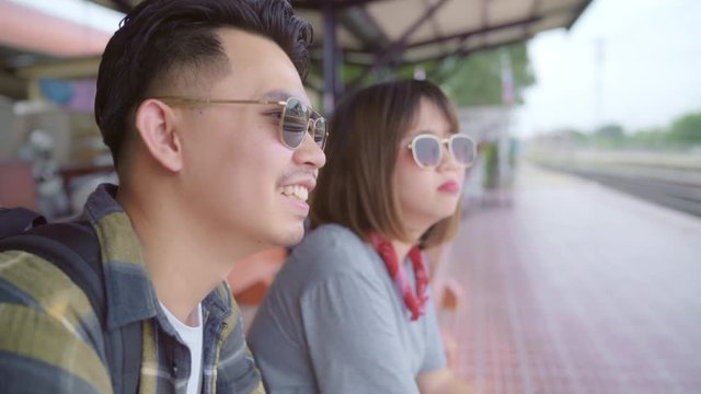 Traveler Asian backpack couple sitting on bench while waiting train, Young sweet couple tourist backpacker enjoy their journey in Thailand. Lifestyles teen couple relax and travel concept.