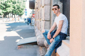 Attractive, sexy guy sits on the street in sunglasses. self-confidence, flatulence and arrogance. model, posing, portrait of a young man