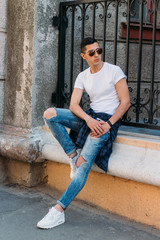 Attractive, sexy guy sits on the street in sunglasses. self-confidence, flatulence and arrogance. model, posing, portrait of a young man