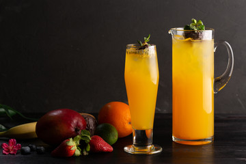 Mango lemonade - passion fruit in a jug and a glass and fruit on a dark wooden background