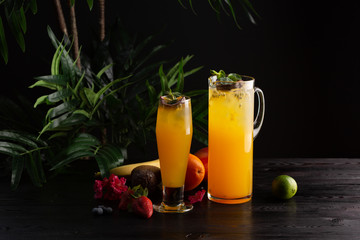 Mango lemonade - passion fruit in a jug and a glass and fruit on a dark wooden background