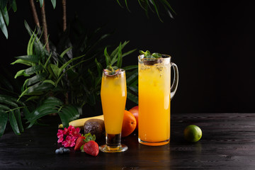 Mango lemonade - passion fruit in a jug and a glass and fruit on a dark wooden background