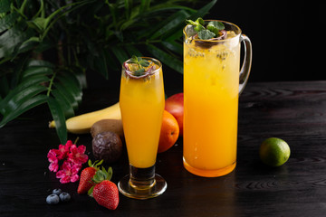 Mango lemonade - passion fruit in a jug and a glass and fruit on a dark wooden background