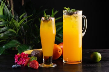 Mango lemonade - passion fruit in a jug and a glass and fruit on a dark wooden background