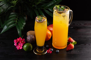 Mango lemonade - passion fruit in a jug and a glass and fruit on a dark wooden background