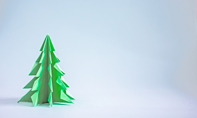 Green origami Christmas tree on a blue background. Background about New Year’s creativity, paper...