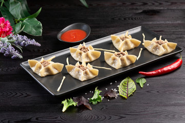 Gyoza with spinach, ricotta and lamb on a black rectangular plate on a dark wooden background