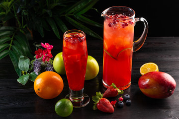 Cranberry lemonade - lingonberries in a jug and glass and fruits on a dark wooden background