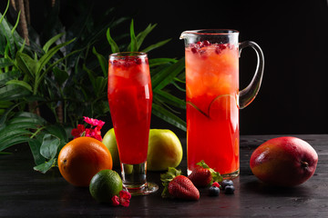 Cranberry lemonade - lingonberries in a jug and glass and fruits on a dark wooden background