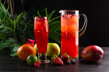 Cranberry lemonade - lingonberries in a jug and glass and fruits on a dark wooden background