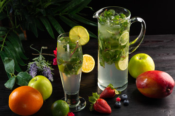 Mojito lemonade in a jug and glass and fruits on a dark wooden background