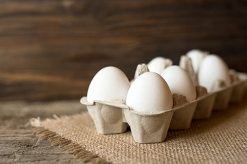 Raw white eggs in egg box on wooden background.