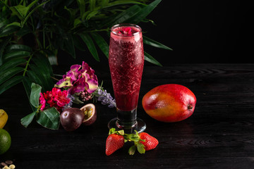 Cocktail with fruits and berries in a tall glass on a dark wooden background