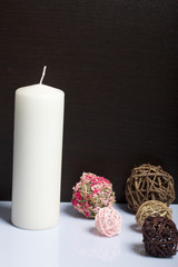 Candle white in color among the decorative balls, woven from natural materials. On a white background.