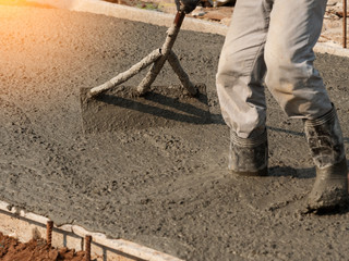 Workers adjust leveling of lean road concrete with hoe