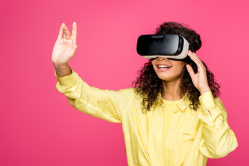 happy curly african american woman wearing virtual reality headset and gesturing isolated on crimson
