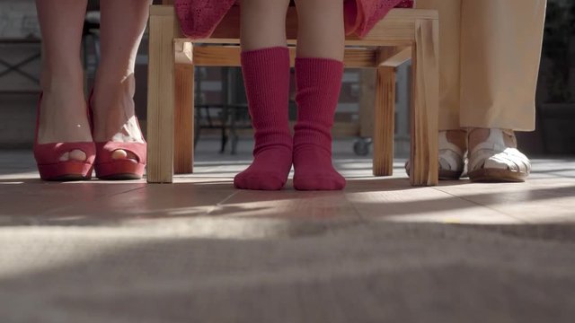 Legs of the mother, little daughter and grandmother. Woman has red shoes, girl stockings and granny beige sandals on their feet. Child sitting on the table. Concept of generations, love, family