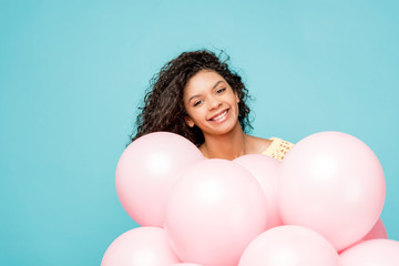 Obraz na płótnie Canvas happy curly african american girl near pink air balloons isolated on blue