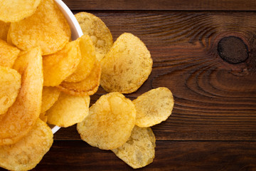 Crispy potato chips in bowl on wooden background, top view