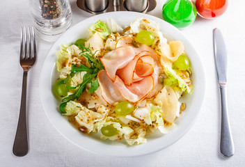 Salad with ham, iceberg, pear, grape and pumpkin seeds on white plate. Close up