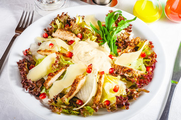 Salad with chicken, greens mix and parmesan cheese on white plate. Close up