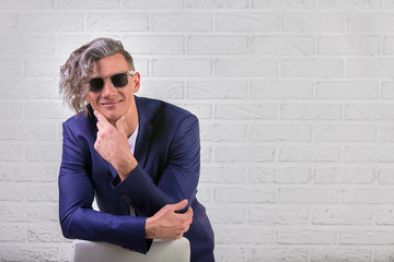 stylish businessman with curly long hair in sunglasses sitting on chair on white background